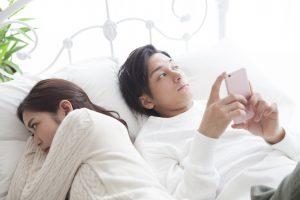 The man is looking at the smartphone in bed